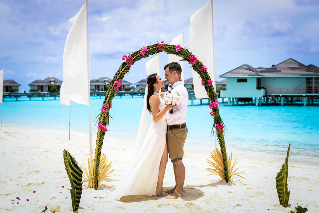 A wedding ceremony on an amazing beach with white sand and a beautiful arch. Against the backdrop of paradise Maldivian bungalows.